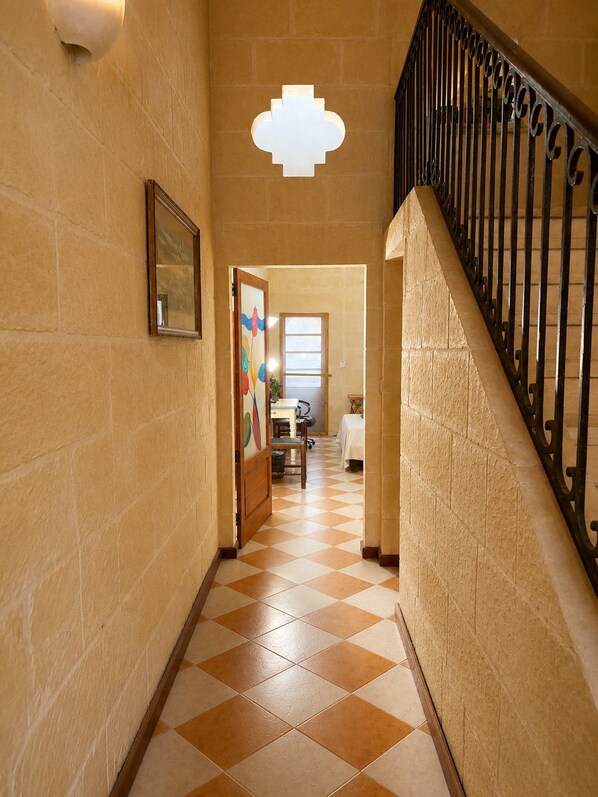 A hallway with a checkered floor, a staircase with a metal railing, and a door with a colorful design.