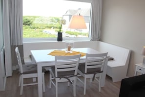 En matplats med ett vitt bord och stolar, ett fönster med utsikt över grönska och byggnader samt en lampa på bordet.