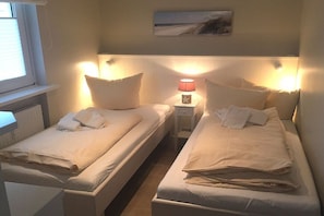Ett dubbelrum med två sängar, var och en med kuddar och ett nattduksbord med en lampa.