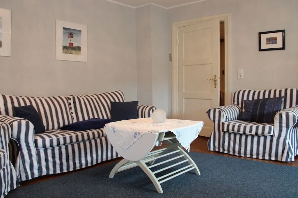Una habitación con un sofá a rayas, una mesita con mantel blanco y una puerta.
