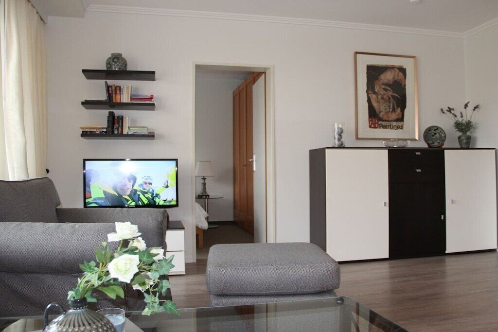 Una sala de estar con un sofá, una mesa de centro de vidrio con un jarrón, un televisor, una estantería y un mueble.
