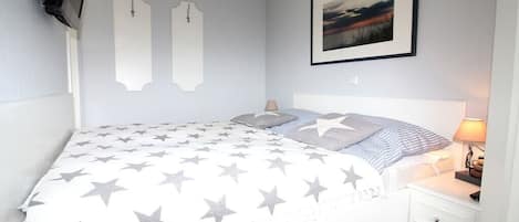 Un dormitorio con una cama, mesitas de noche, un televisor montado en la pared y un cuadro enmarcado.
