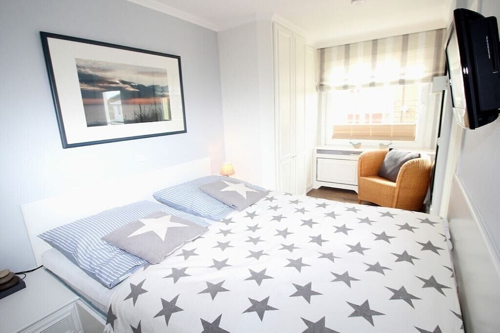 A bedroom with a bed, a chair, a television, and a window with curtains.
