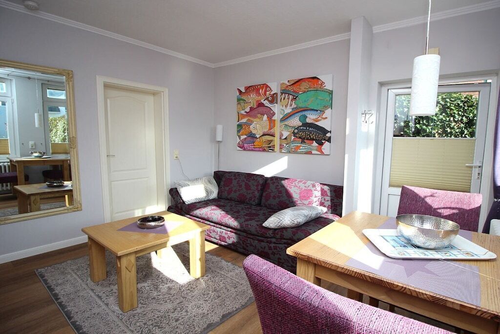 Un salon comprenant un canapé, une table basse en bois, une table à manger avec des chaises, un tapis et un mur orné d’œuvres d’art colorées.