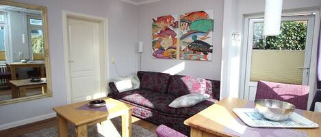 Un salon comprenant un canapé, une table basse en bois, une table à manger avec des chaises, un tapis et un mur orné d’œuvres d’art colorées.