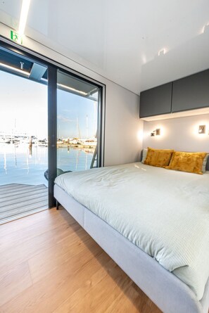 Un dormitori modern amb un llit gran, vista a un port esportiu i una porta corredissa a l'exterior.