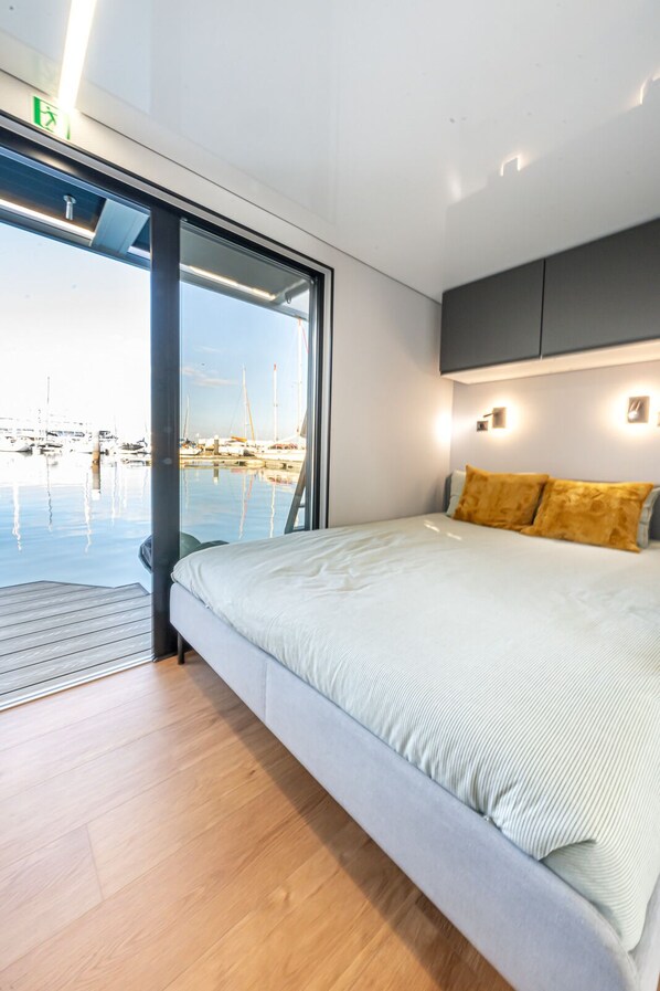 A modern bedroom with a large bed, a view of a marina, and a sliding door to the outside.