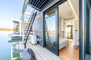 A modern boat interior with a glass door leading to a deck area, a ladder, and a small table with a chair.