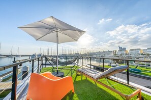 A terrace with a view of a marina, featuring a hammock, a lounge chair, and an umbrella.