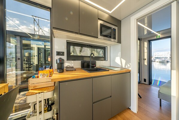 A modern kitchen with a built-in microwave, a coffee machine, and a sink. There is a window providing a view of the marina.
