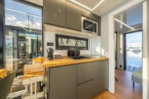 A modern kitchen with a built-in microwave, a coffee machine, and a sink. There is a window providing a view of the marina.