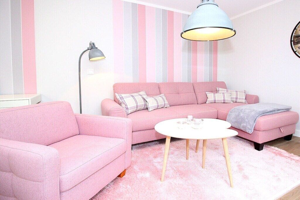 A pink sofa with a matching armchair, a small round table, and a floor lamp in a room with striped wallpaper.