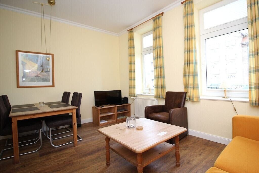 Een gemeubileerde woonkamer met een houten tafel, stoelen, een bank, een televisie en een raam met gordijnen.