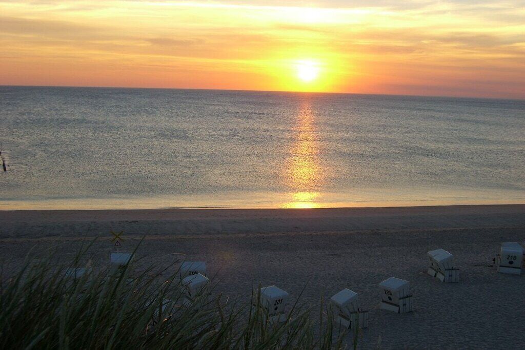 A beach with a sunset, clear sky, and several beach huts.