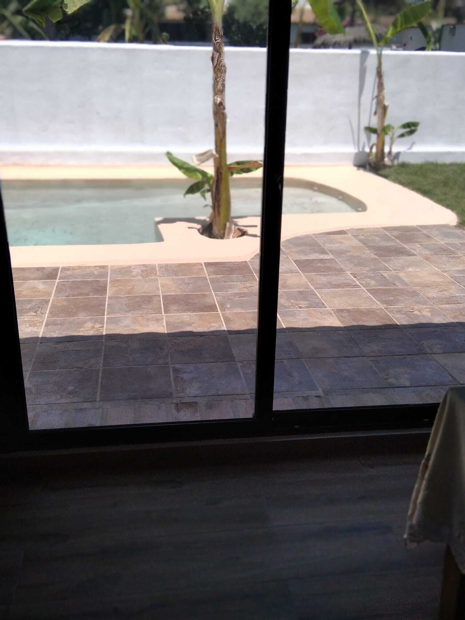 A view of a swimming pool with tiled flooring and a white wall in the background.