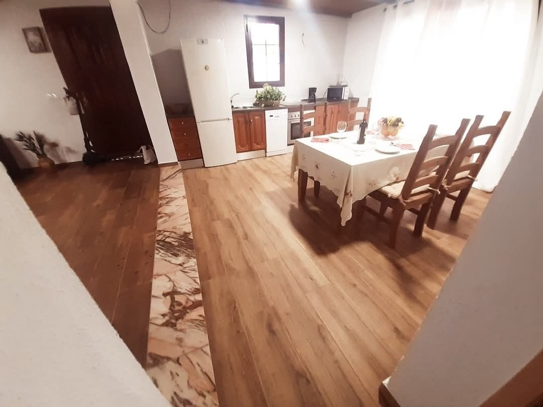 Uma área de refeições com mesa e cadeiras, uma cozinha com eletrodomésticos e um piso de madeira.