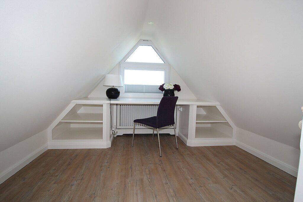 A room with a sloped ceiling, a window, a desk with a chair, and built-in shelving.