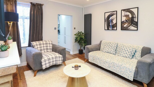 A modern living room with a grey sofa, a plaid armchair, a round coffee table, and abstract art on the wall. - Regents Cottage (Melton Mowbray)
