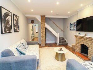 Ein Wohnzimmer mit einer Couch, einem Couchtisch, einem Kamin und einem an der Wand befestigten Fernseher.