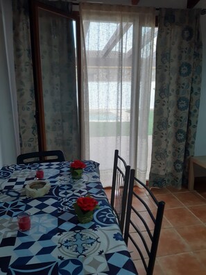 A dining area with a table set for two, featuring a patterned tablecloth, two chairs, and a vase with red flowers. - Villa Margarita    . (Chiclana de la Frontera)