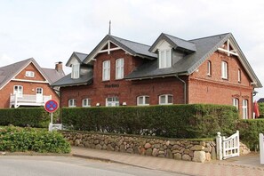 En byggnad av rött tegel med en vit grind, en skylt som förbjuder parkering och en mur av sten.