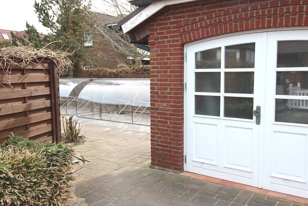 Ein Backsteinhaus mit einer weißen Garagentür, einem Holzzaun und einem Gewächshaus im Hintergrund.