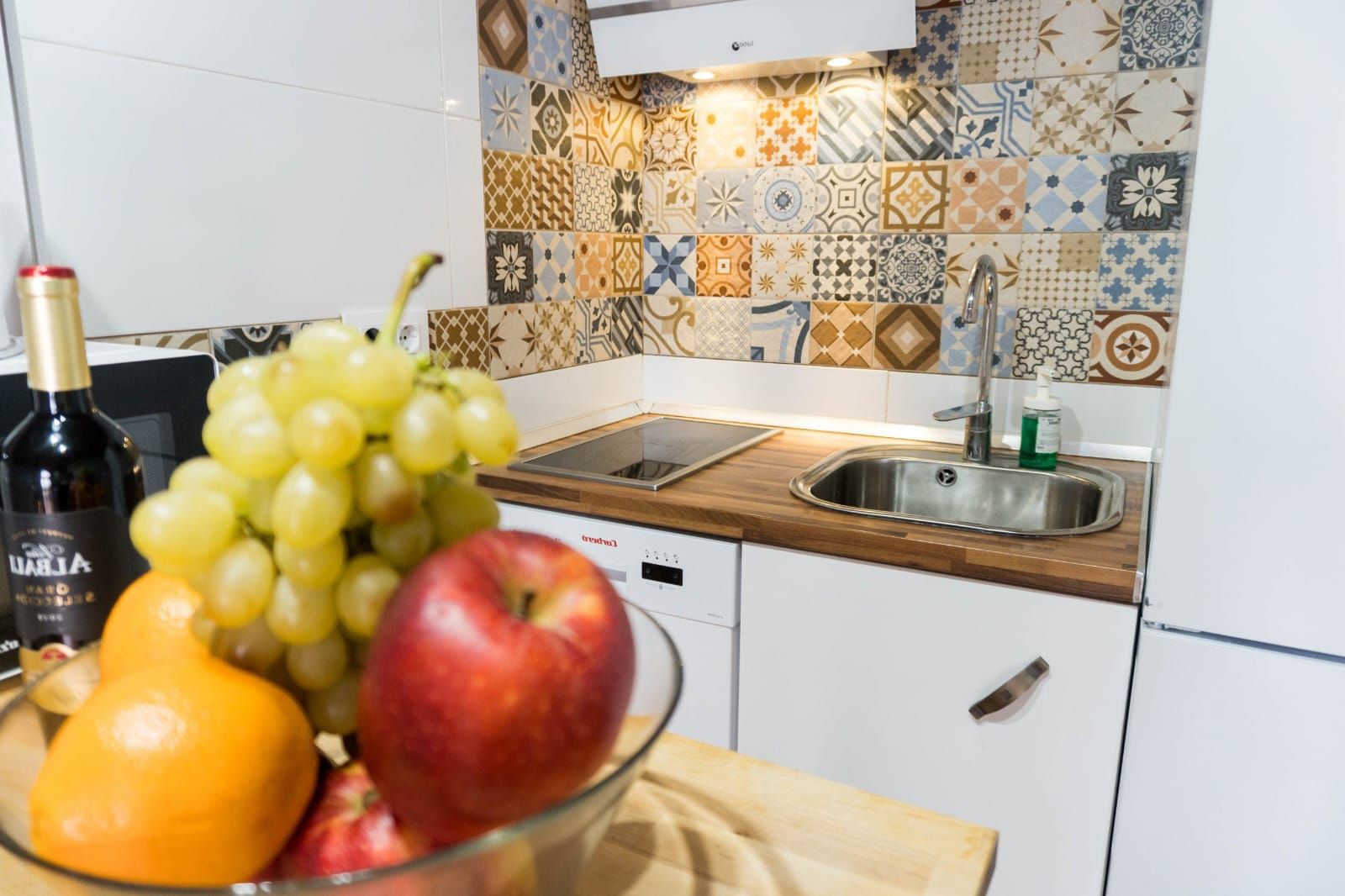 Una cocina con salpicadero de azulejos, un lavabo y un bol de fruta en la encimera.