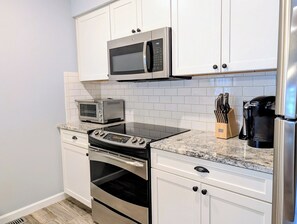 A kitchen with white cabinets, a microwave, a toaster, a stove, and a coffee maker. - Sea Colony 3BR Condo w/ Blue Screened Porch & Resort Amenities (Bethany Beach)