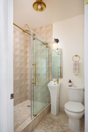 Een badkamer met een douche met glazen wand, een witte wastafel en een toilet.