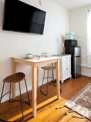 Een kleine keuken met een houten tafel, twee barstoelen, een televisie, een magnetron en een koelkast.