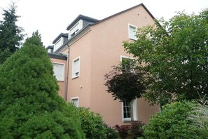 A multi-story residential building with a flat roof, white window shutters, and a variety of surrounding greenery. - Arndt Holiday Apartment (Dresden Weißer Hirsch)