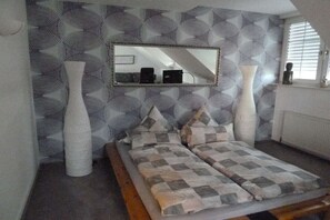 A bedroom with a bed, two large vases, a mirror, and patterned wallpaper. - Arndt Holiday Apartment (Dresden Weißer Hirsch)
