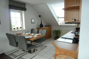 A compact kitchen with a dining area, a window with plants, and a built-in oven. - Arndt Holiday Apartment (Dresden Weißer Hirsch)