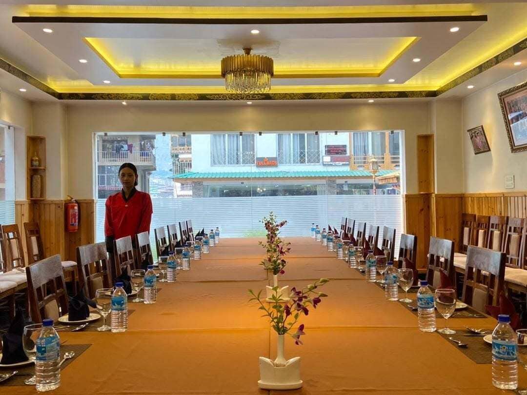 Un salón de conferencias con una mesa larga, sillas, botellas de agua y un jarr ón con flores.