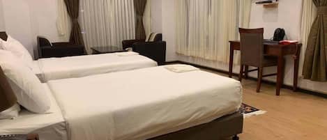 A hotel room with two beds, a desk, a chair, a TV, and curtains.