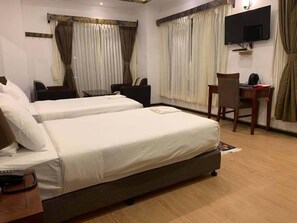 Une chambre d’hôtel avec deux lits, un bureau, une chaise, une télévision et des rideaux.