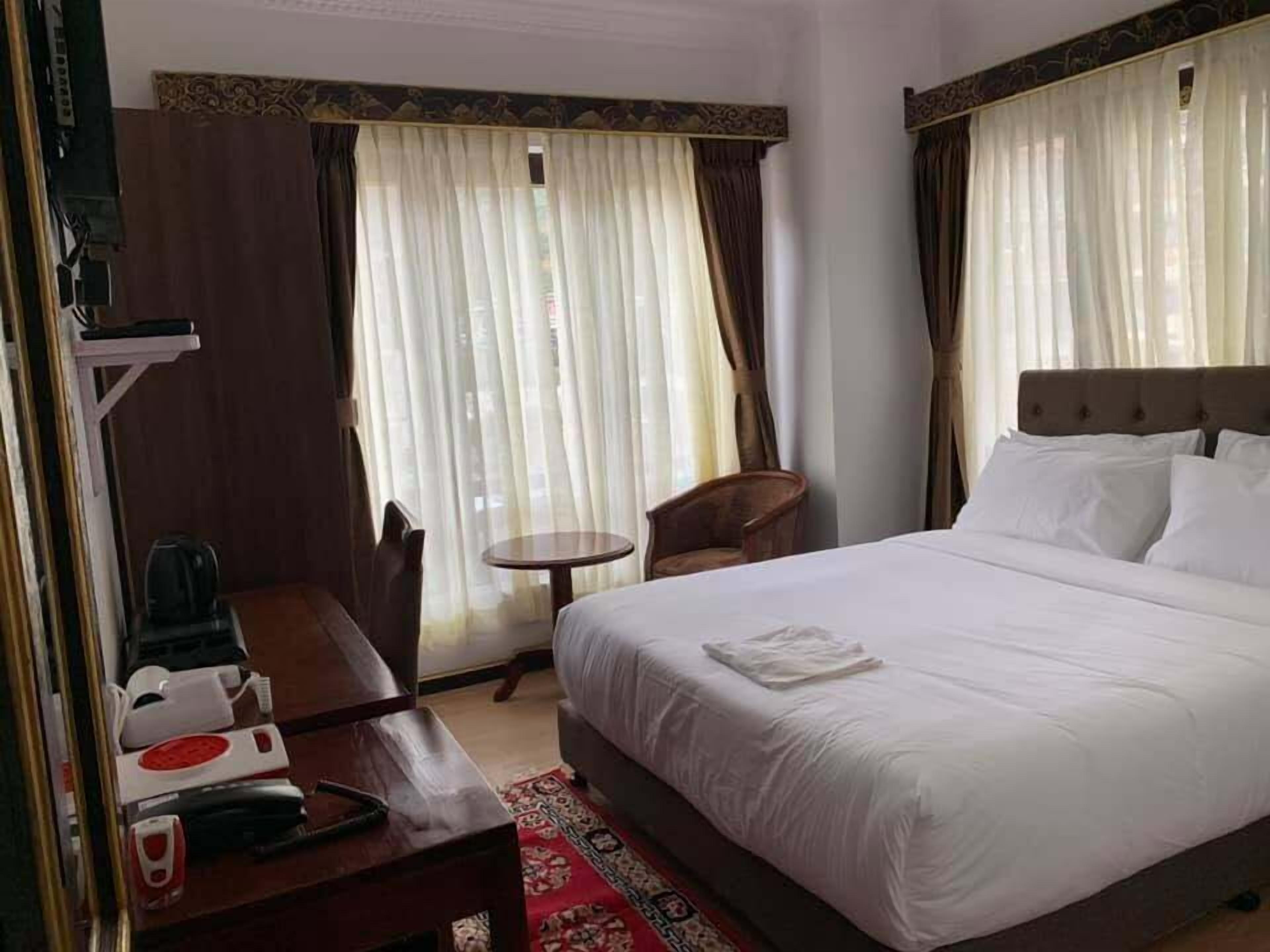 Habitación de hotel con cama, escritorio con teléfono, una silla y una pequeña mesa.