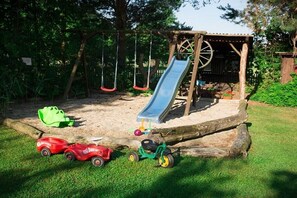 A playground with a slide, swings, and a small green tricycle. - Stein - Apartment Spreewald (Byhleguhre)