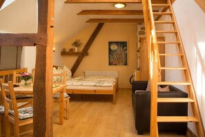 Ein Schlafzimmer mit einem hölzernen Bett, einem kleinen Schreibtisch, einem Stuhl, einer Leiter und einem Bild an der Wand.