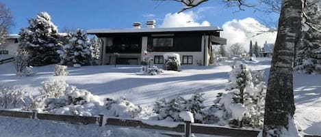 Une maison moderne à deux étages, avec une allée et un paysage environnant recouverts de neige.