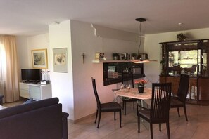 Ein modernes Wohnzimmer mit Fernseher, einer Couch und einem Essbereich mit Tisch und Stühlen.
