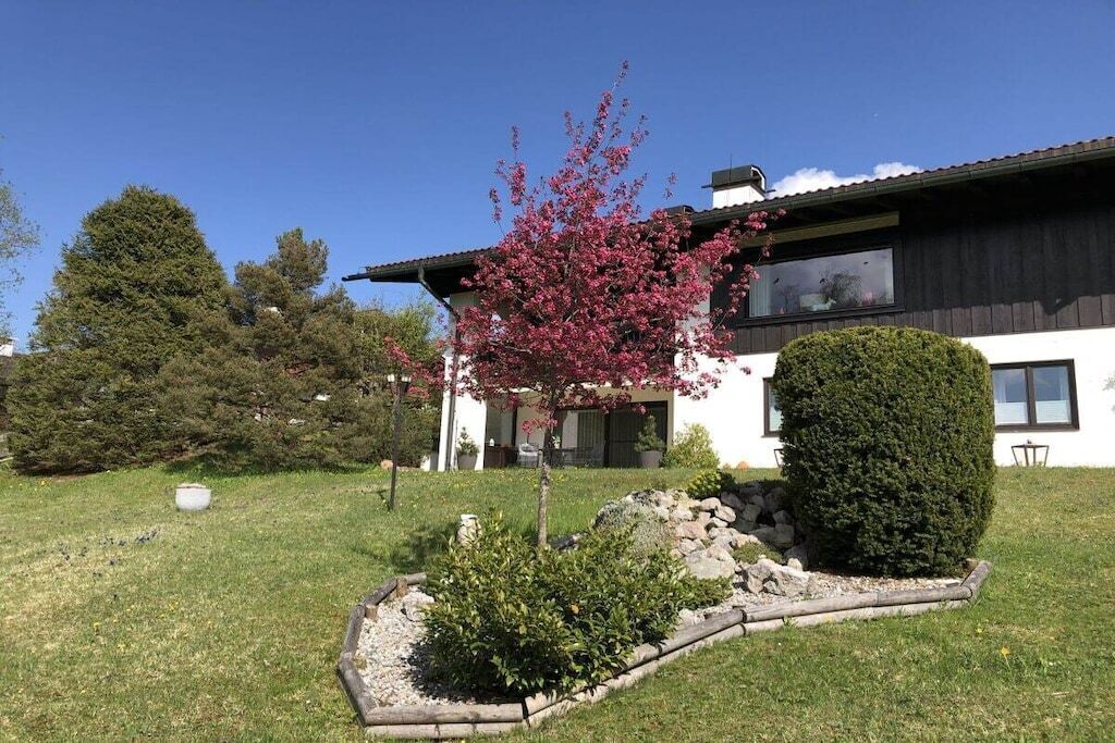 A modern two-story house with a well-maintained garden, including a flowering tree and a neatly trimmed hedge.
