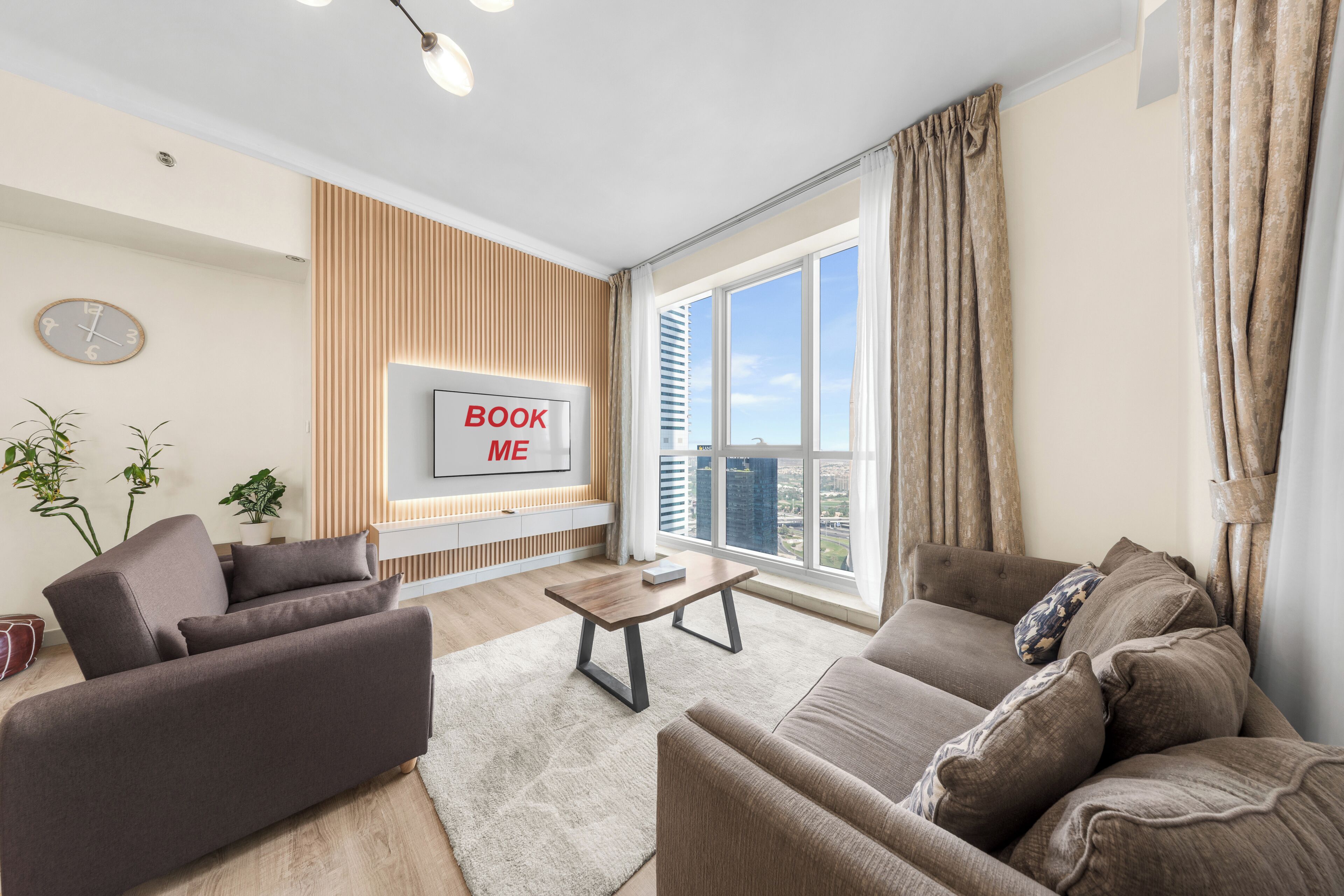 A modern living room with a large window, a mounted TV, and a 'BOOK ME' sign.