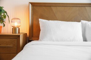 En pænt redt seng med hvide sengetøj, et træhovedgærde og en sengetlamps.