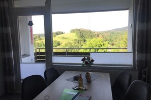 A dining area with a table set for two, a window with a view of a green landscape, and a hanging decoration. - Holiday apartment with 2 bedrooms (Altenau)