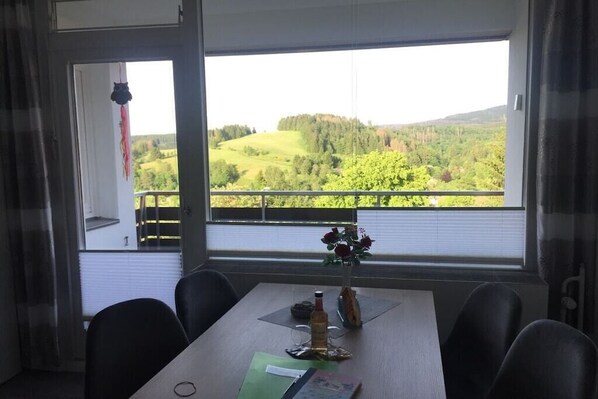 A dining area with a table set for two, a window with a view of a green landscape, and a hanging decoration. - Holiday apartment with 2 bedrooms (Altenau)