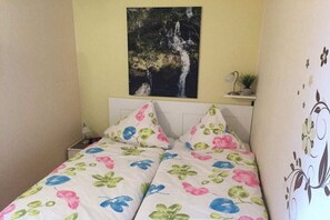 A bedroom with a bed, a nightstand, a wall-mounted shelf with a plant, and a painting of a waterfall. - Holiday apartment with 2 bedrooms (Altenau)