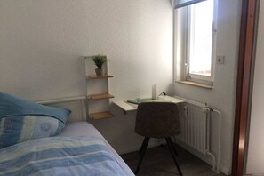 A bedroom with a bed, a desk, a chair, a radiator, and a window. - Holiday apartment with 2 bedrooms (Altenau)