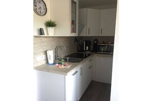 A compact kitchen with white cabinets, a sink, a clock, and a potted plant. - Holiday apartment with 2 bedrooms (Altenau)