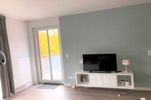 Ein Zimmer mit einer großen Schiebeglaswand, einer weißen Unterhaltungsanlage inklusive Flachbildfernseher und einem kleinen Tisch mit einer Lampe.